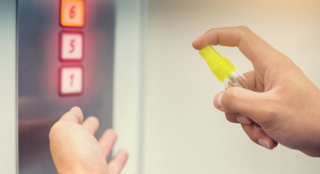 Person Spraying Hands with Disinfectant on Elevator